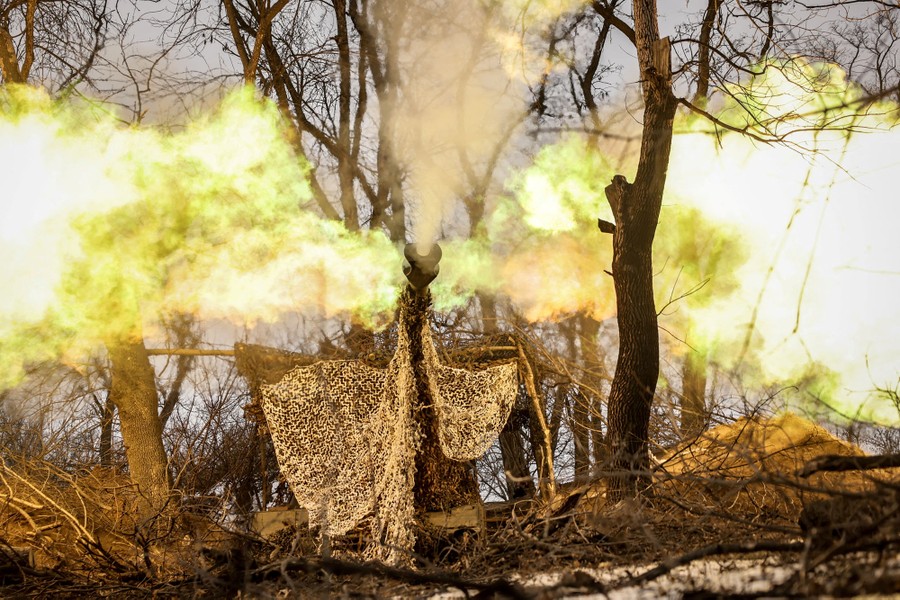 Flames and smoke erupt from the muzzle of a howitzer as it is fired from a stand of trees.