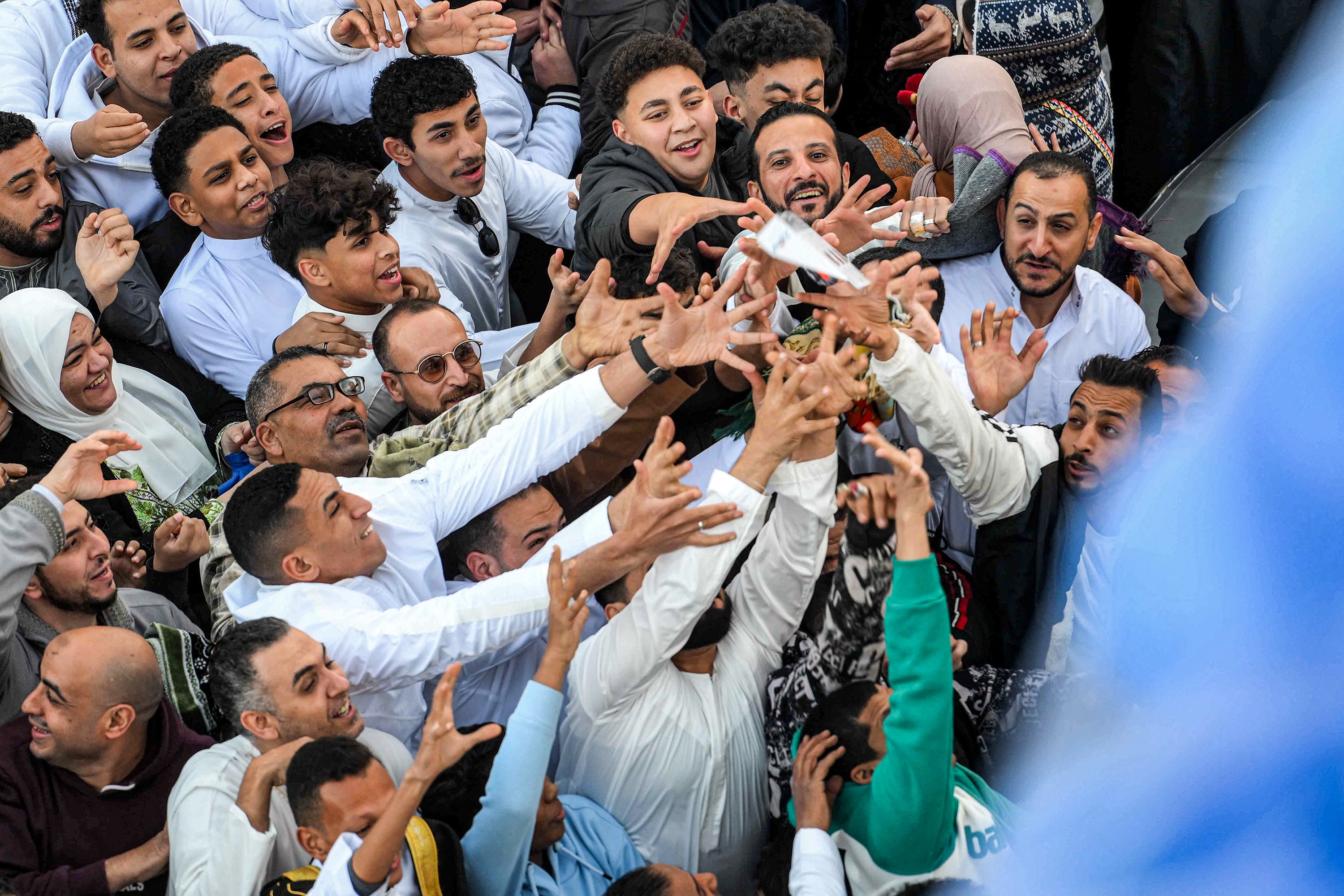 People crowd together, reaching up to receive gifts being handed out.