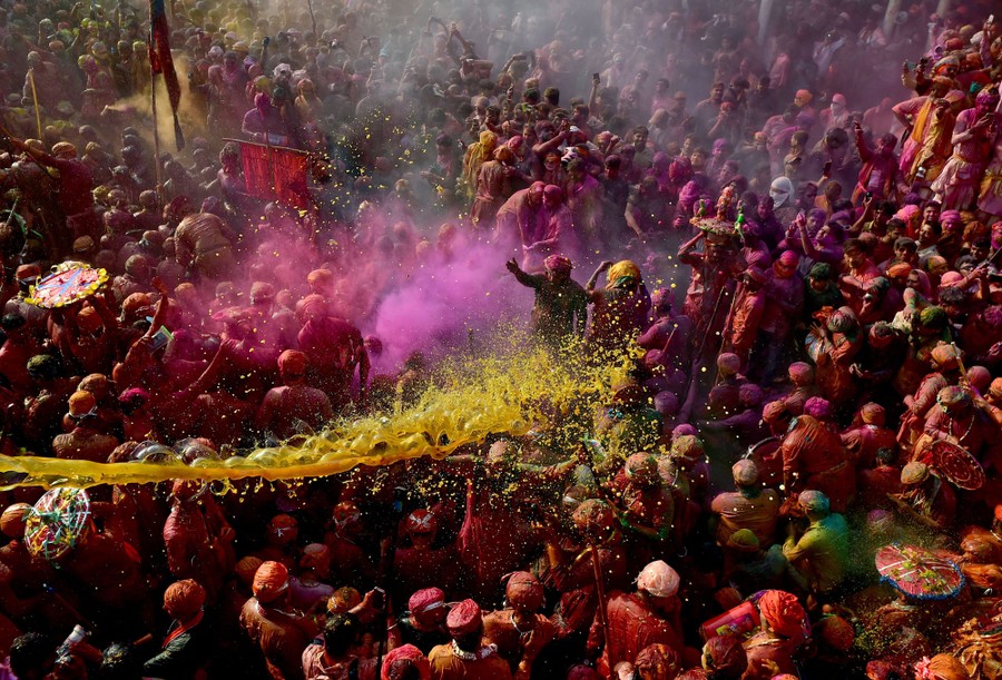 A large crowd of celebrating people throw colored powder and colored water.