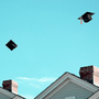 An illustration of graduation caps being thrown above houses.