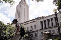 A student walks in front of a clock tower at UT Austin