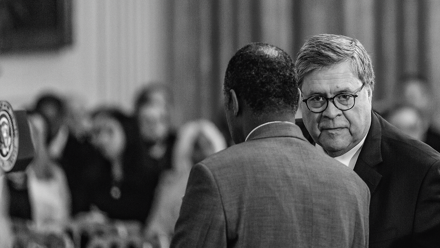Fotografía en blanco y negro de Bill Barr y Ben Carson conversando, con la audiencia de fondo.