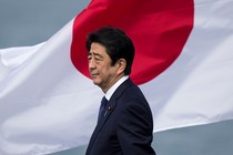 Former Japanese Prime Minister Shinzo Abe, wearing a navy suit and standing in front of the Japanese flag