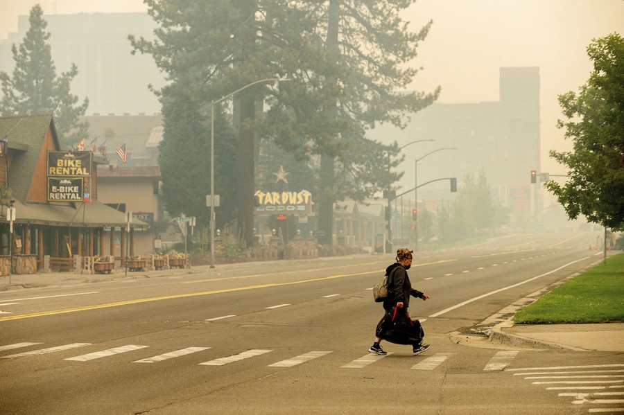 A person crosses an empty street beneath a smoky sky.