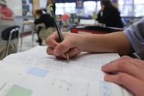 A student writes with pencil on a sheet of notebook paper.