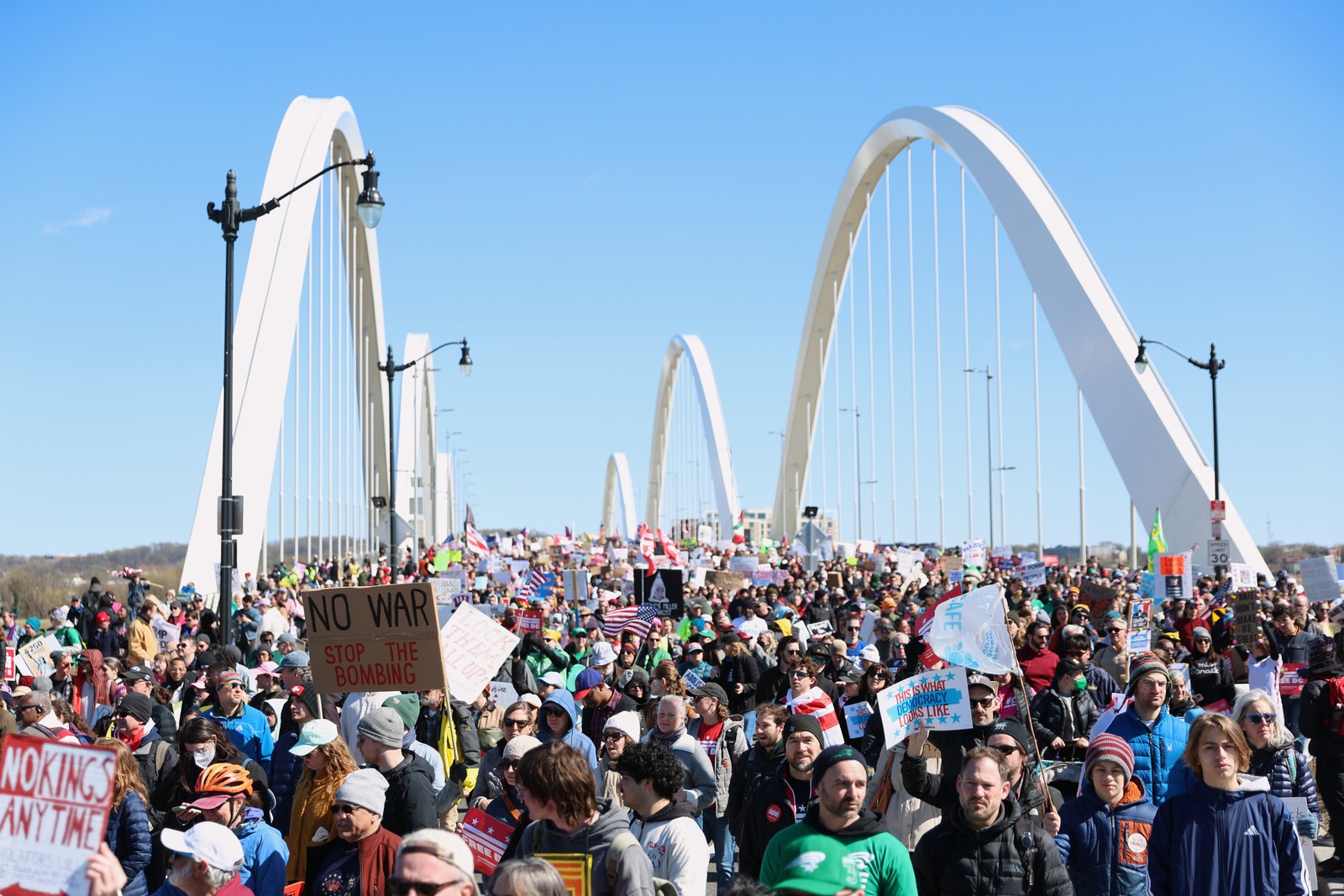 Protesters carry signs as they walk across a road bridge.