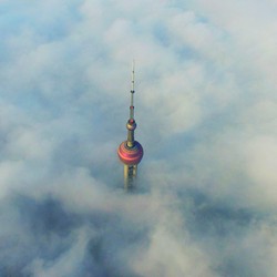 The spire of a skyscraper rising above a a bed of clouds