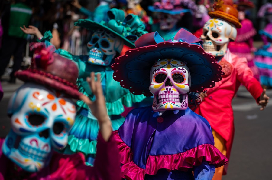 Performers in skeletal costumes march in a parade.