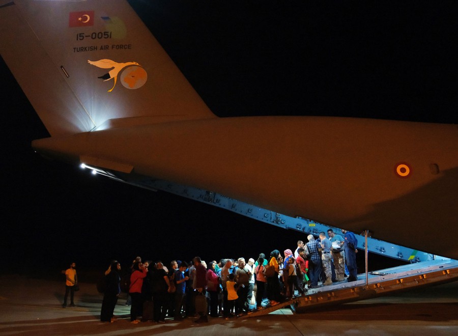 A group of people stand at the bottom of a ramp leading into a large military aircraft.