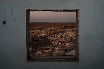 The wreckage of a neighborhood is framed by the empty window frame of an abandoned Palestinian home.