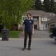 A color film still from "Final Destination Bloodlines" where a man stands in a suburban street, while a big truck approaches behind him from the right.