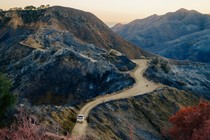 A car drives up a dirt road winding up a Los Angeles mountain that is burned from fire.