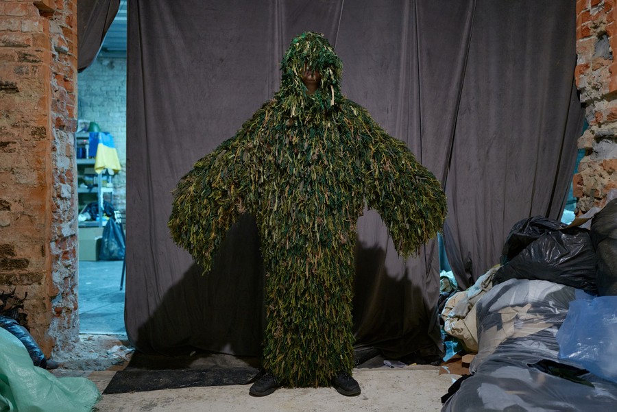 A person stands in a room, wearing a shaggy full-body camouflage suit.