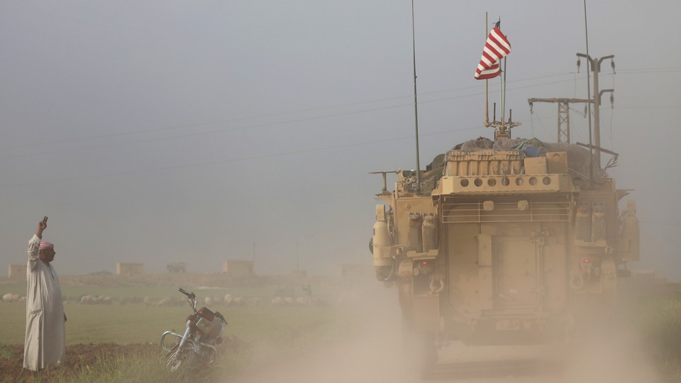A man gestures at U.S. military vehicles driving in the town of Darbasiya in Syria.