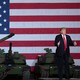 Donald Trump standing in front of tanks and an American-flag backdrop