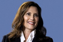 A photo of Gretchen Whitmer smiling against a blue background