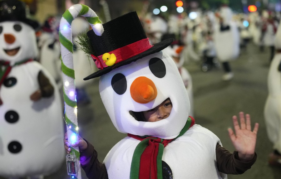 Children dressed in Frosty the Snowman costumes dance during a Christmas parade.