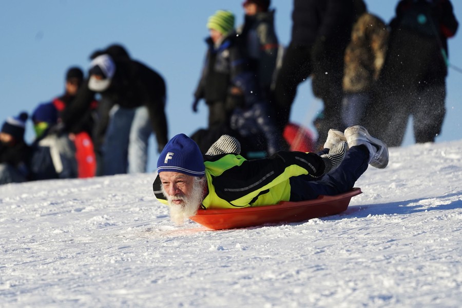 A man sleds down a hill as others stand nearby.