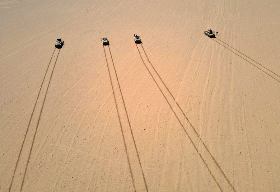 An aerial view of four military vehicles and their tracks in a desert