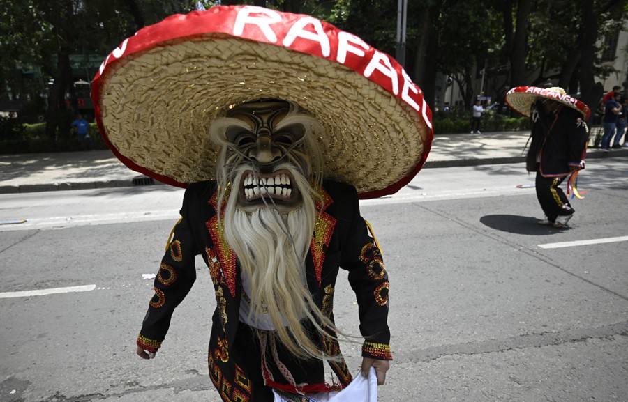 A person wearing a costume and a frightening mask walks in a march on a city street.
