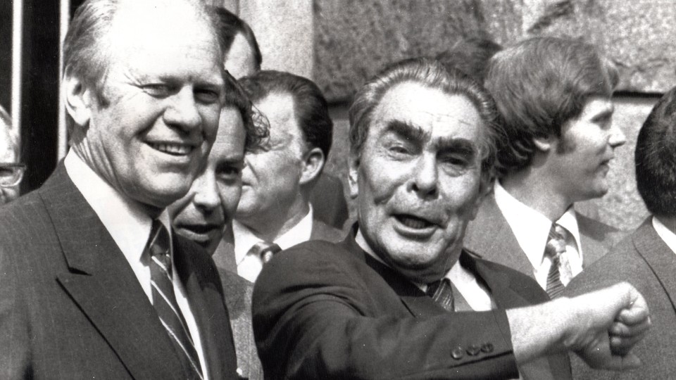 President Gerald Ford and Leonid Brezhnev smile in the foreground, while translator Victor Sukhodrev and Jan Lodal stand in the background.