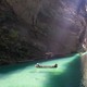 People ride small boats on clear water in a tall and narrow canyon.