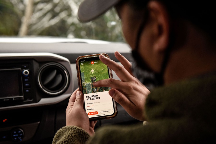 A person sits in a vehicle, checking a map-based tracking app on their phone.