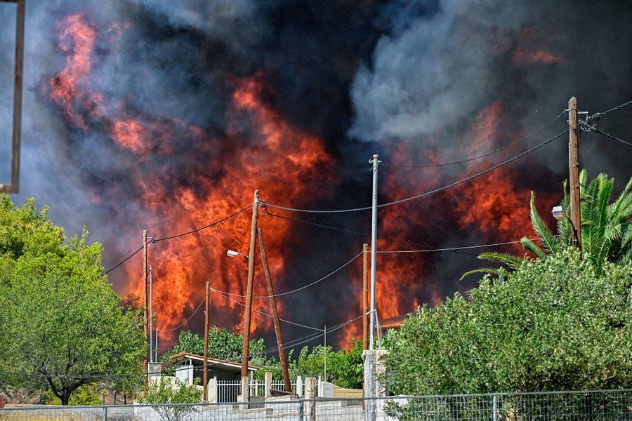 Large plumes of fire and smoke rise in the background of a residential neighborhood.