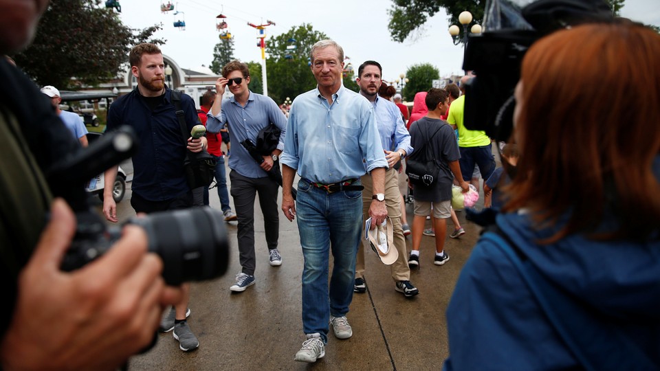 The Democratic presidential candidate Tom Steyer walks through the Iowa State Fair in Des Moines. People are surrounding him. One person, in the foreground, is pointing a camera at him.