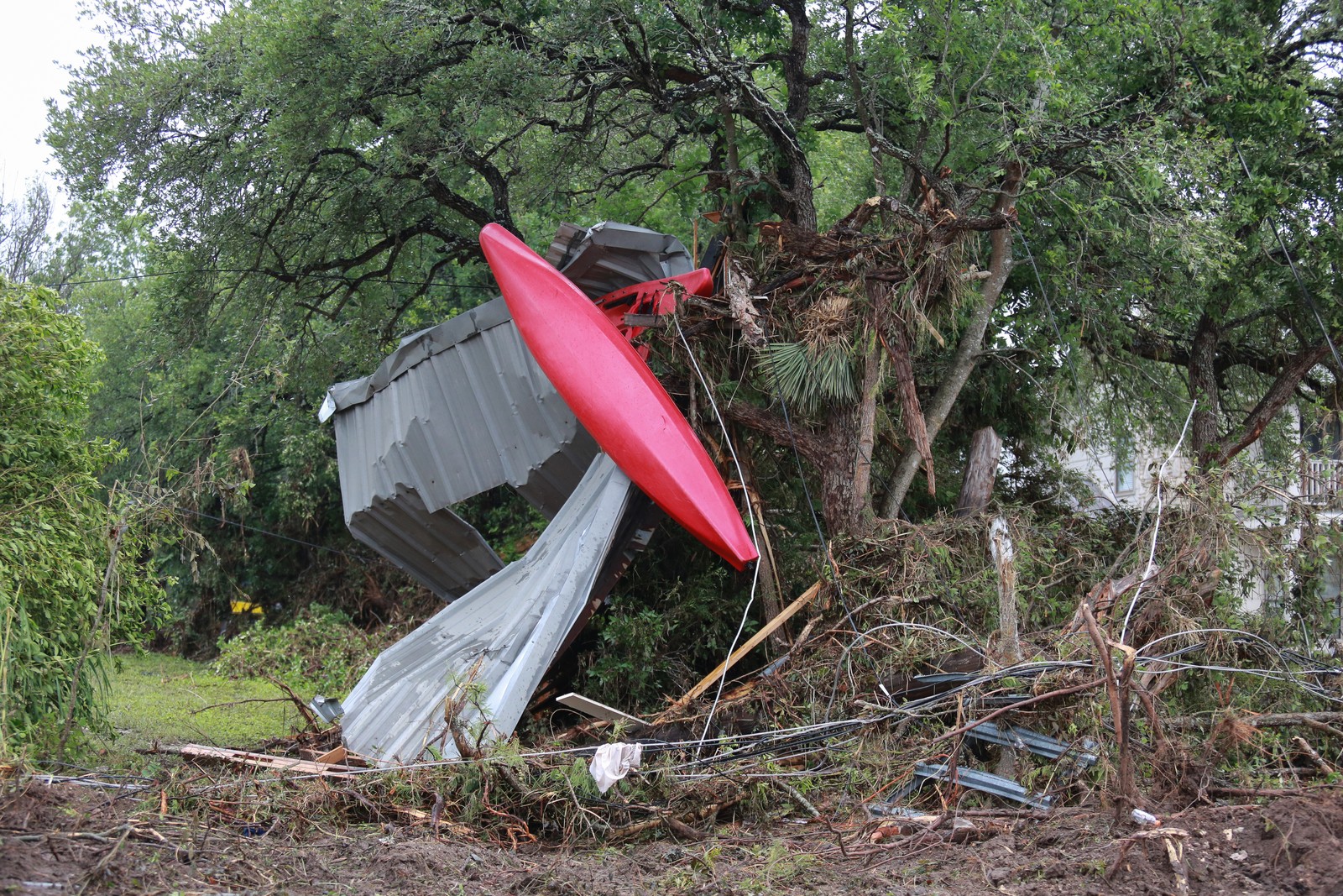 Flood debris, including kayaks, sheet metal, lumber, and branches, lies tangled in trees.
