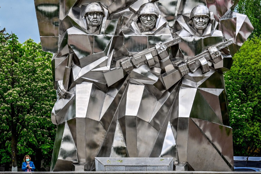 A woman stands next to a large stainless-steel World War II–era monument.