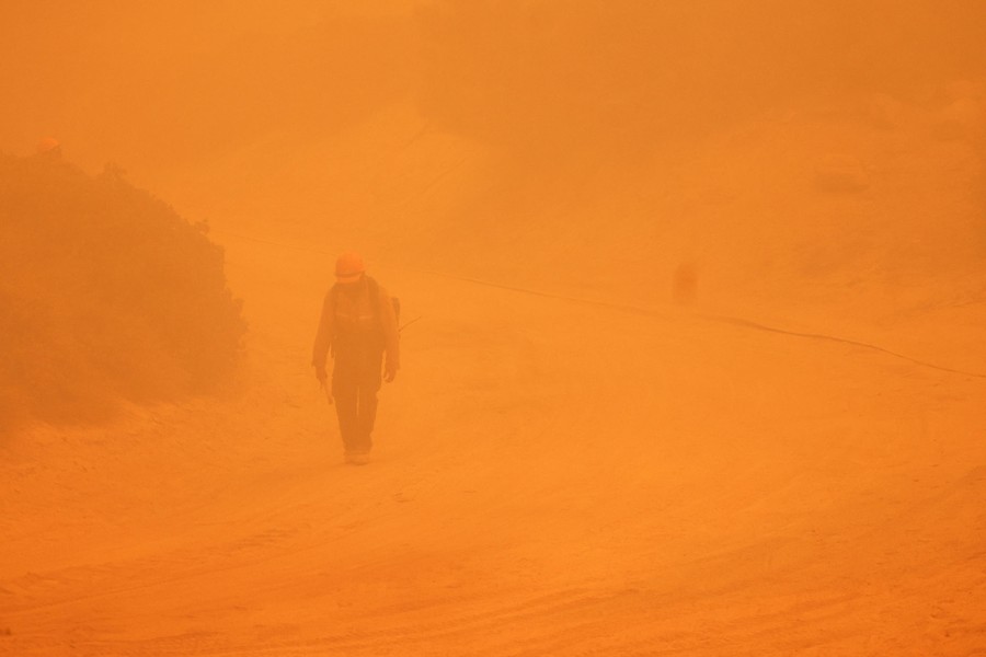 A firefighter walks through smoky air on a road.