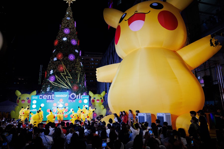 Dancing Pikachus perform on a stage in front of a Christmas tree and a giant inflatable Pikachu.