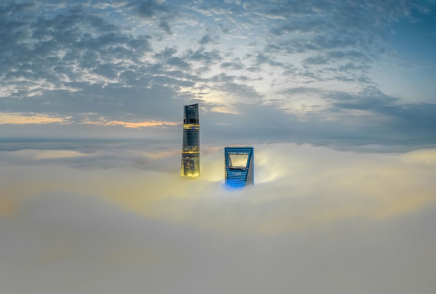 The tops of two tall buildings poke out of dense fog.