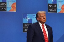 Trump stands alone at a NATO summit in front of a blue background