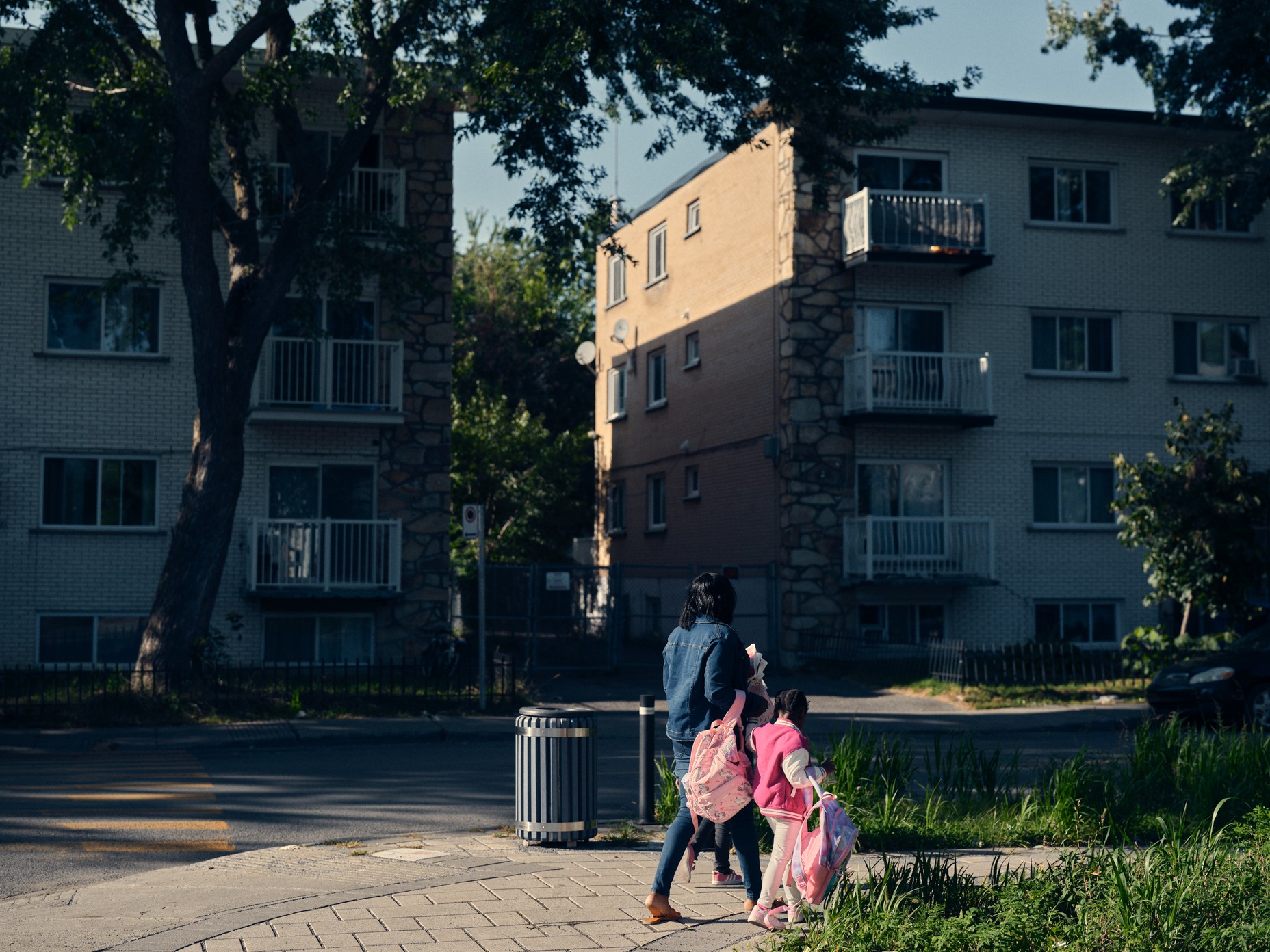 a woman and girl walk in front of apartment buildings