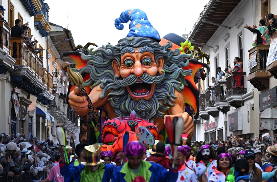 Costumed people parade in front of a large colorful float in the shape of a wizard.