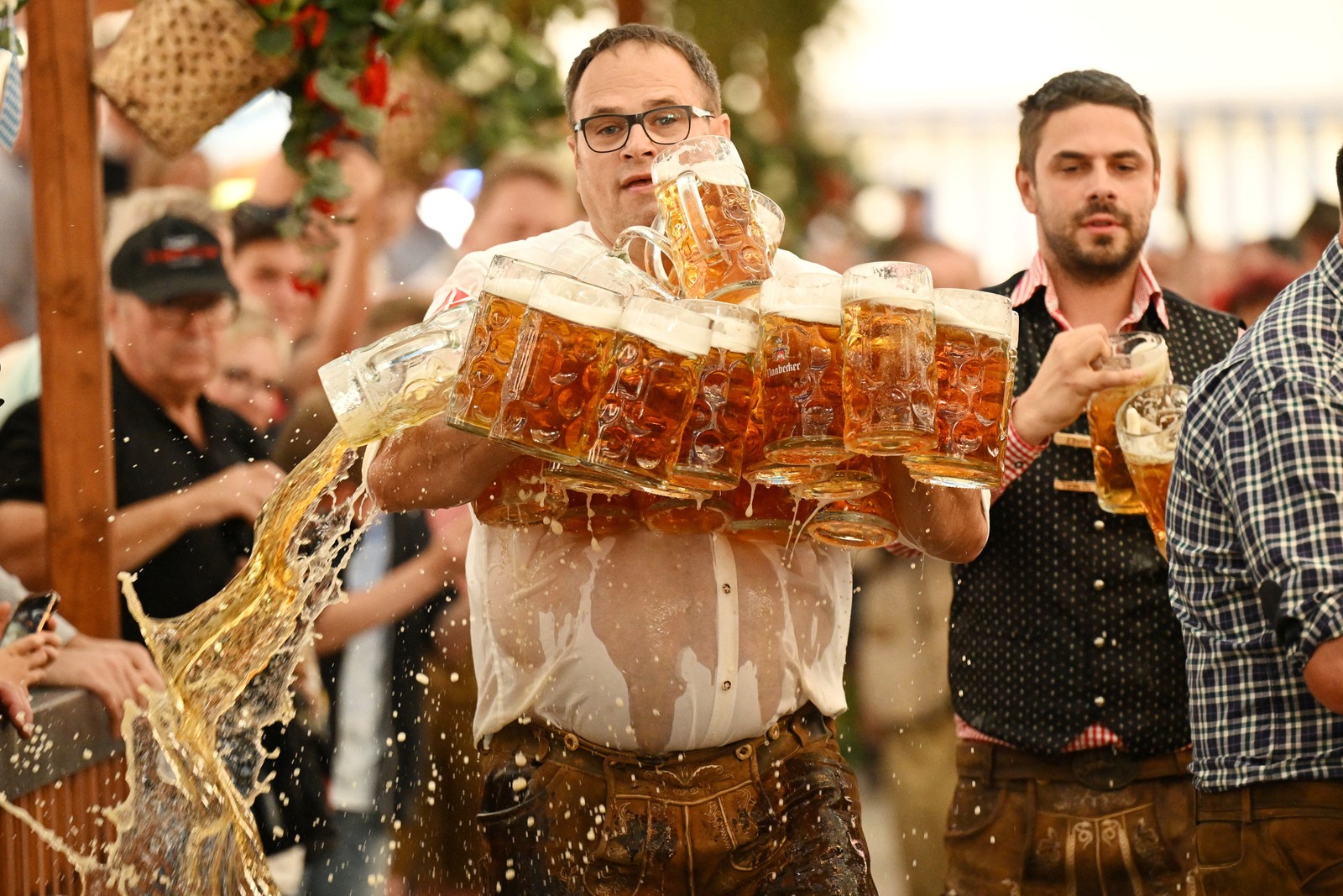 A man carrying more than 30 full beer mugs spills one or two.