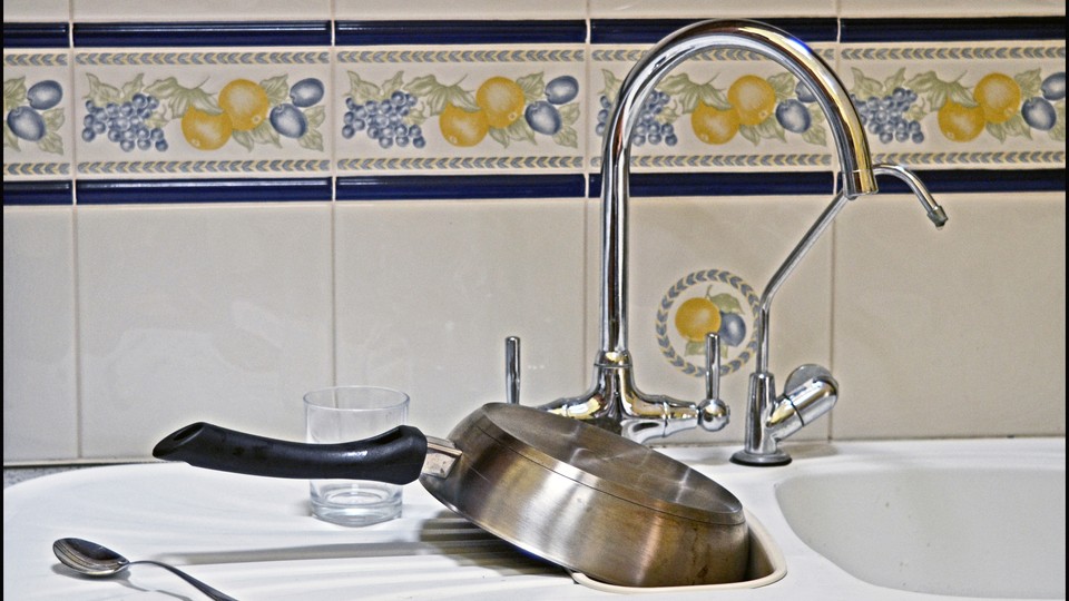 A kitchen sink with a pan, a glass, and a spoon sitting on the counter next to it.