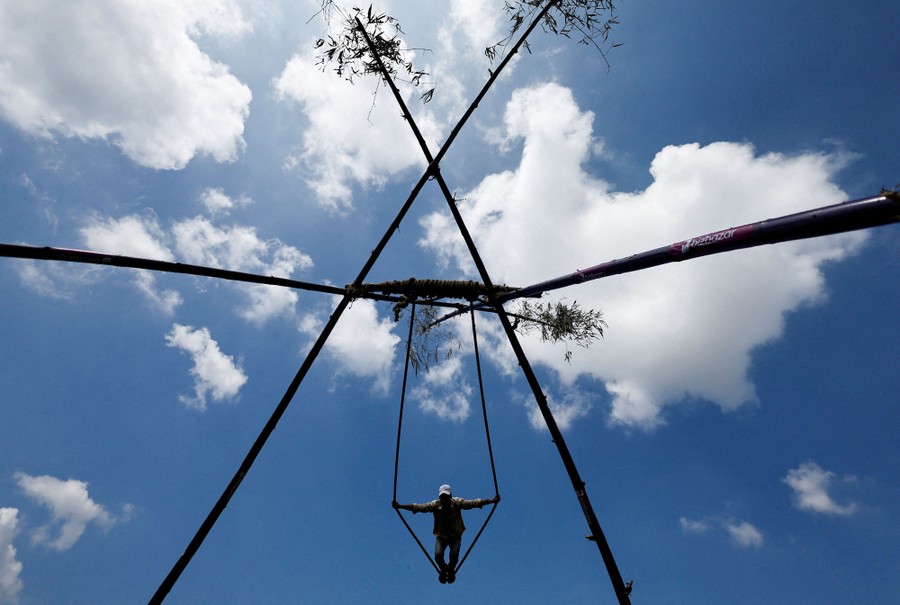 A view looking up, from beneath a swing supported by four long bamboo poles