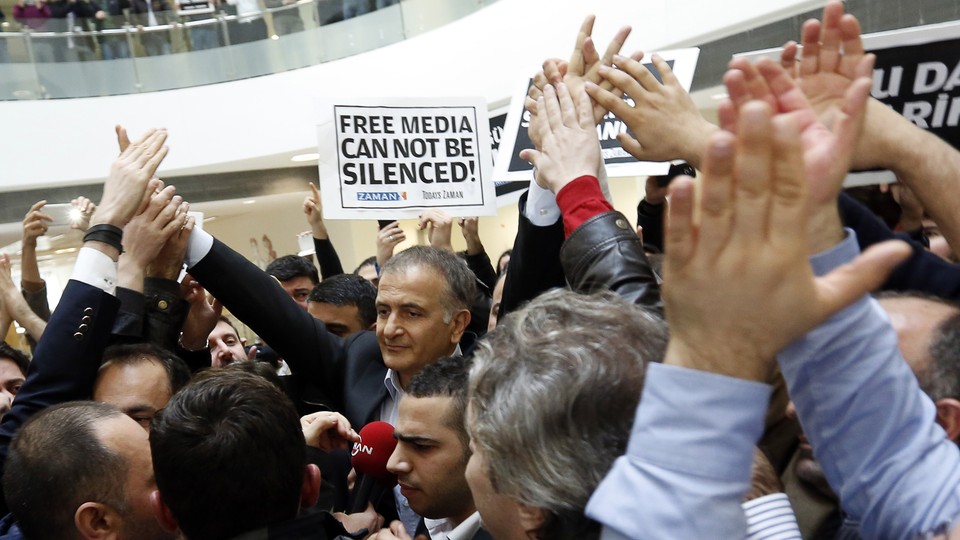 The Zaman editor in chief, Ekrem Dumanli, stands in a crowd of supporters and newspaper employees holding signs that say, in English and Turkish, "Free media cannot be silenced."
