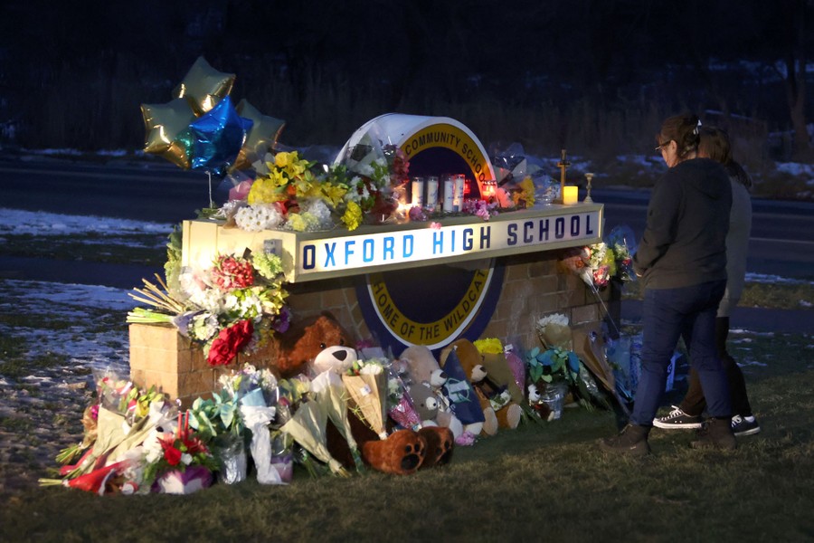 People look at a makeshift memorial, where flower bouquets have been placed beside a sign bearing the name of a high school.