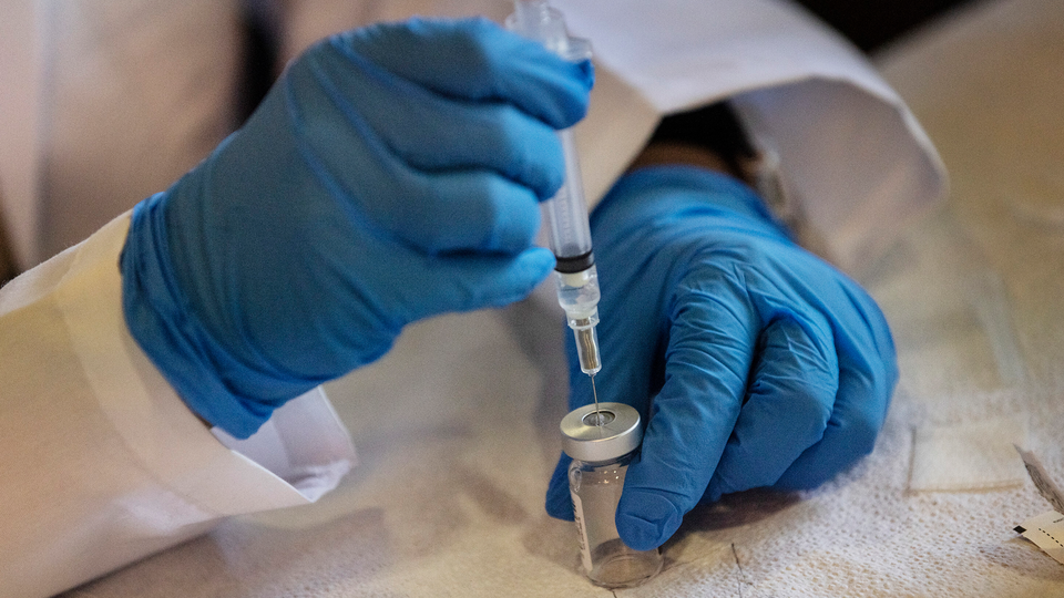 A syringe pulling a vaccine from a vial