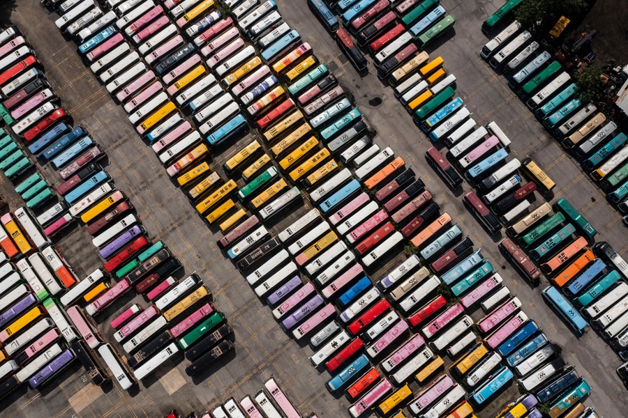 Dozens of colorful tour buses in a parking lot are seen from above.