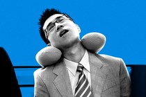 A businessman asleep on public transport using a neck pillow