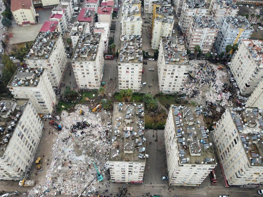 An aerial photo showing two collapsed buildings among a dozen or so identical apartment buildings.