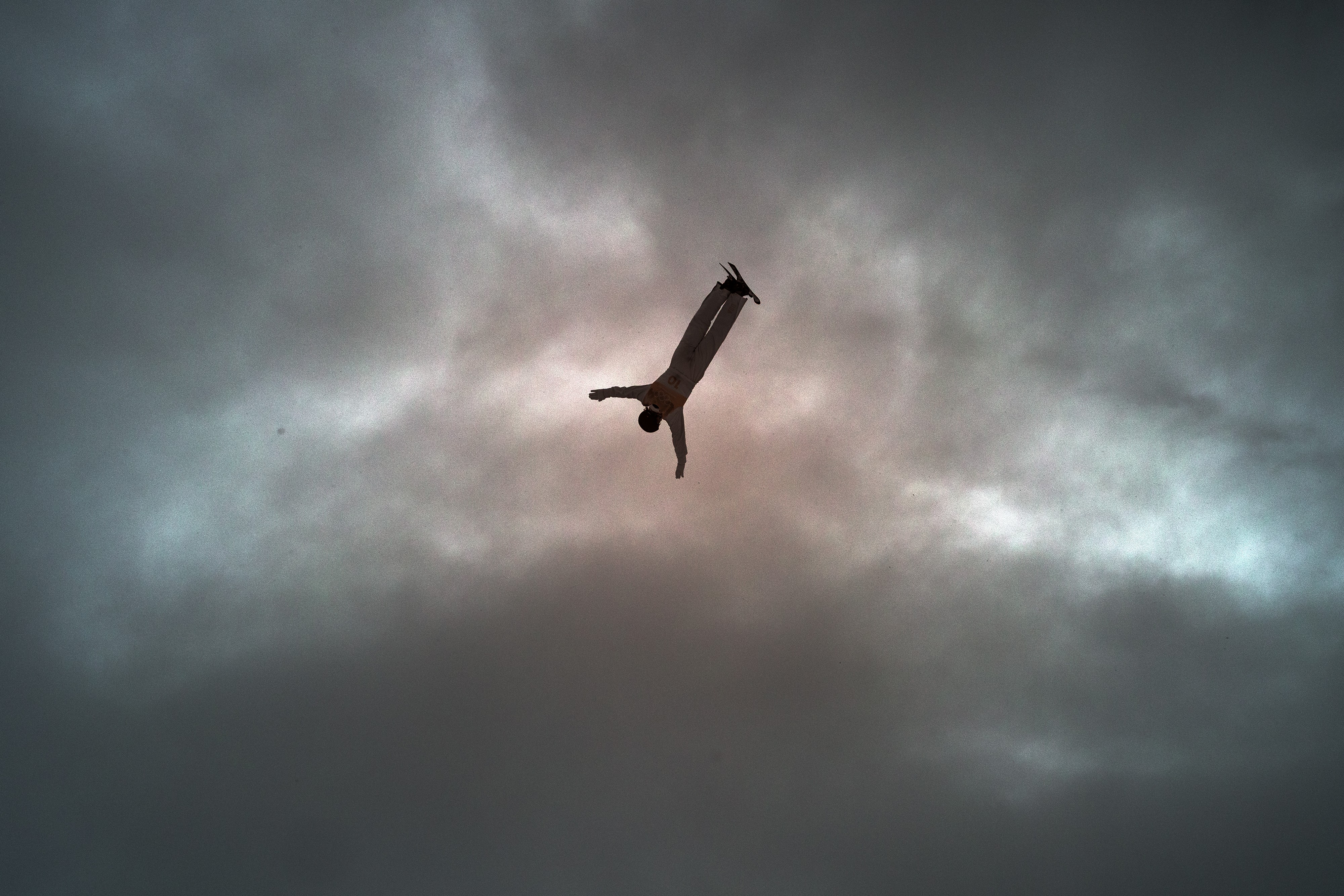 A skier, seen mid-jump, high in a cloudy sky, during a competition