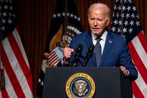 Joe Biden stands at a podium in front of American flags and holds one hand in a fist