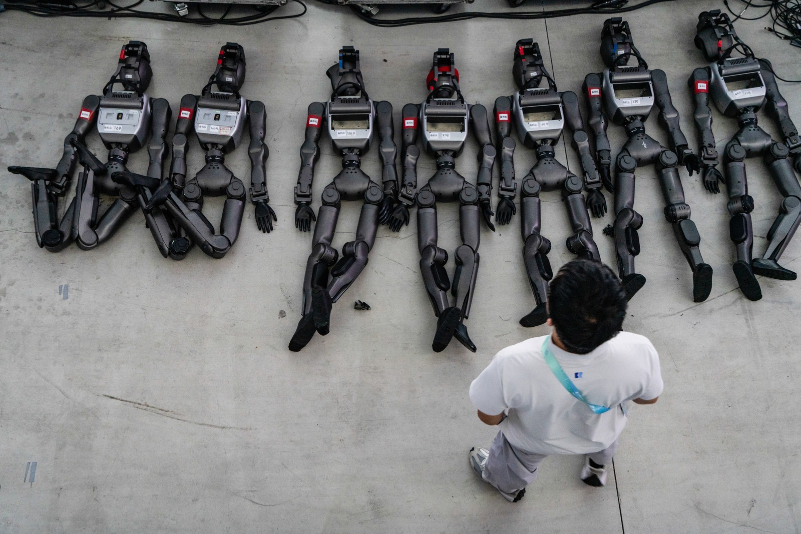 A person stands over seven humanoid robots that lie on concrete.