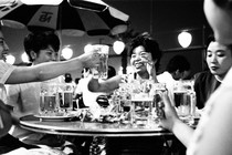 a black-and-white image of Asian women, seated around a table, toasting each other with mugs of beer